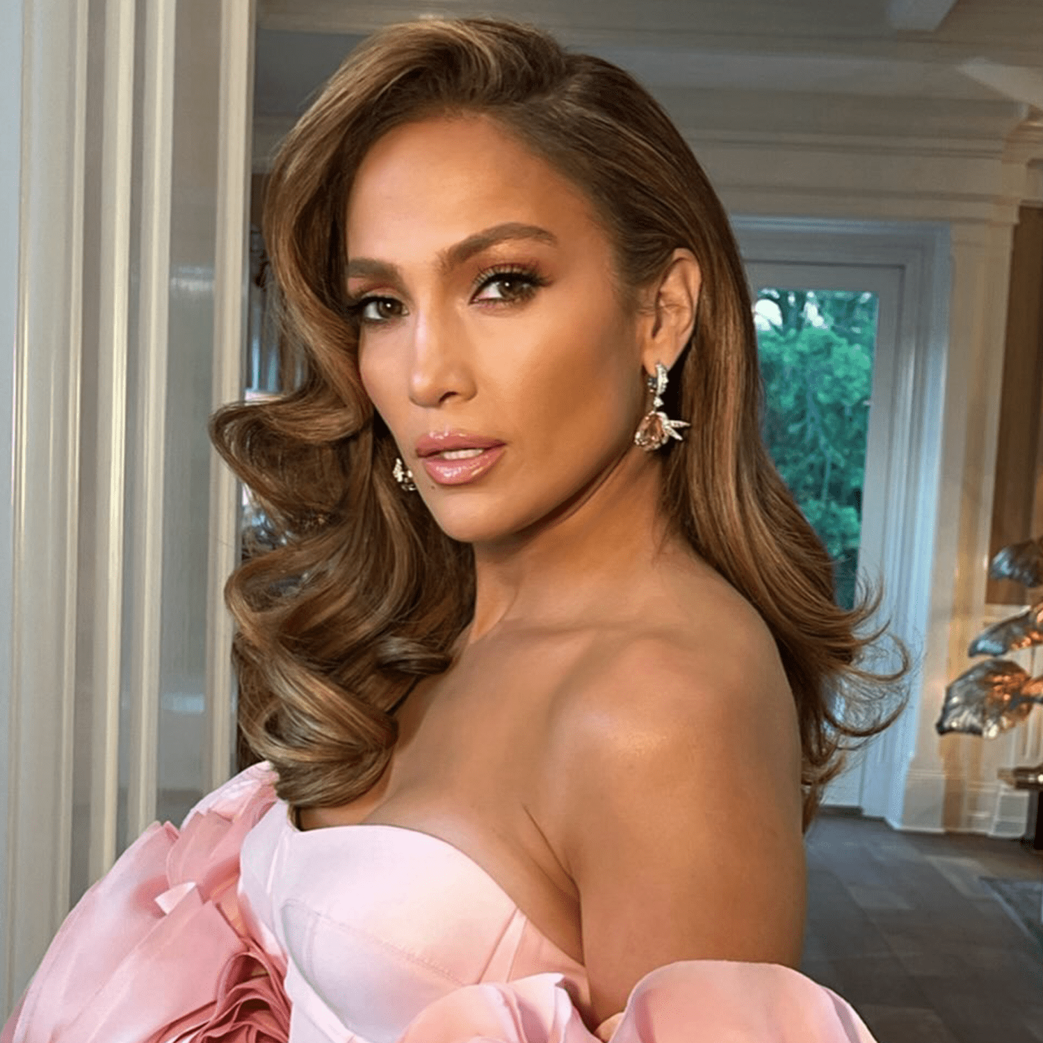 Jennifer Lopez w teksturyzowanych włosach układających się w fale w pudrowo różowej sukni